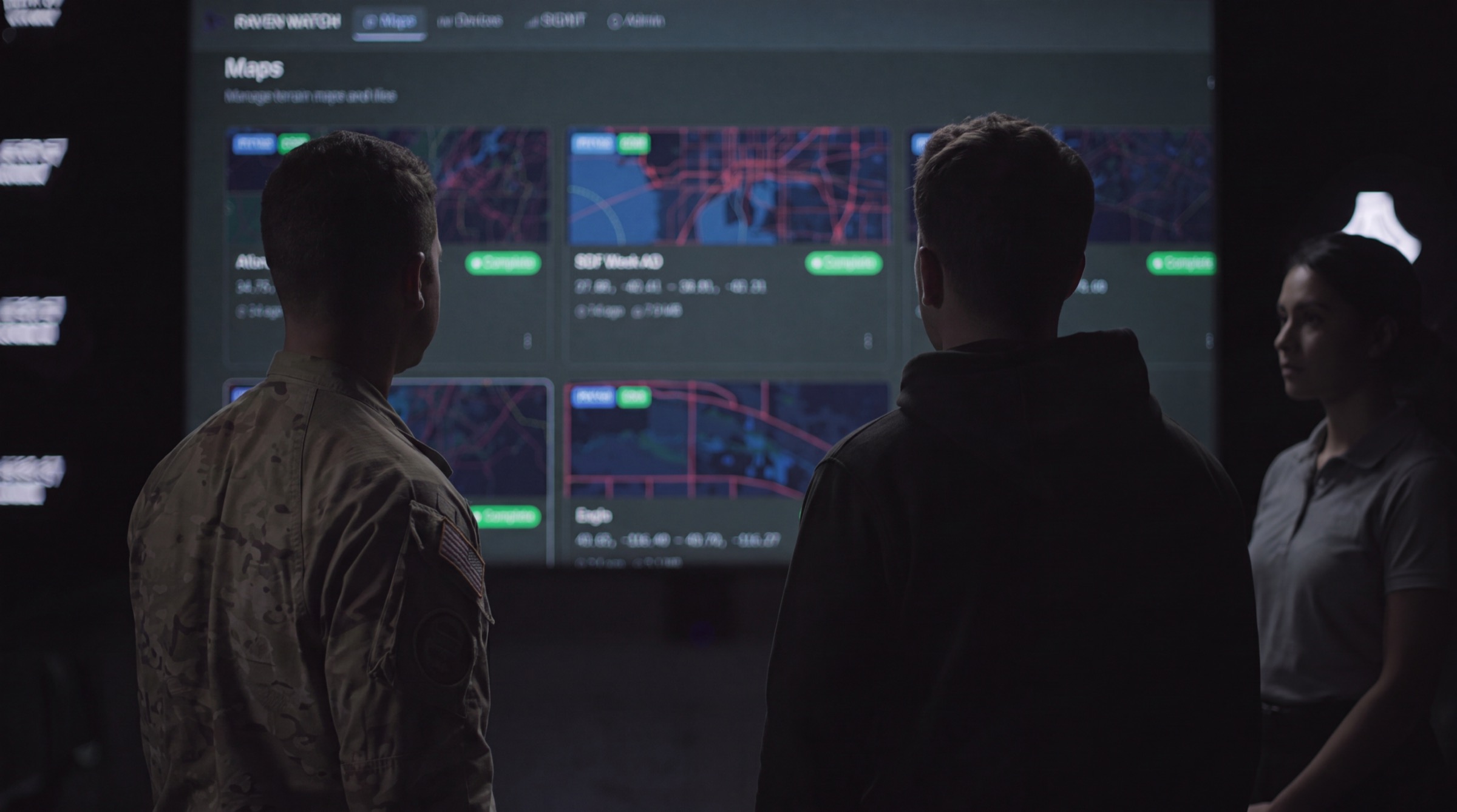 Three operators standing before a wall-sized Raven Eye common operational picture